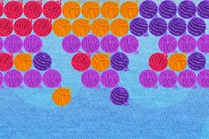 Farebné guľôčky zoradené v radoch na modrom pozadí, zahŕňajúce červené, oranžové, fialové a purpurové odtiene