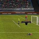 Futbalista kopajúci loptu cez rozhodcu a brankára na ihrisku s divákmi na tribúnach