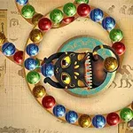 Farebná reťaz guľôčok obklopuje tmavú mačaciu sochu s otvorenou tlamou na pozadí s egyptskými hieroglyfmi